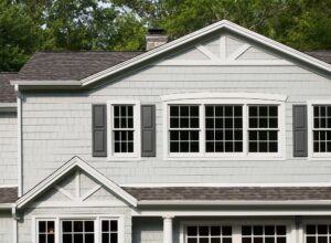 Light gray two-story home with dark gray shutters and asphalt shingle roofing. White double-hung and picture windows on second floor